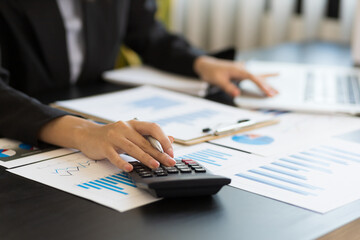 Fototapeta premium Close-up woman hand press calculator to calculate the company's financial results On the wooden table in the office and business work background, tax, accounting, statistics, and analytical research.