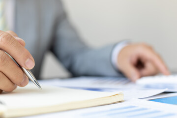 Businessman writing notes on financial reporting notepad and working using desk calculator, tax, accounting, statistics and statistical analysis concepts.