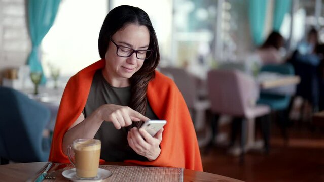charming woman is viewing pictures in social media and resting in coffee shop, drinking latte
