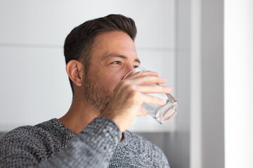 Man drink water from glass indoors looking away - 490543048