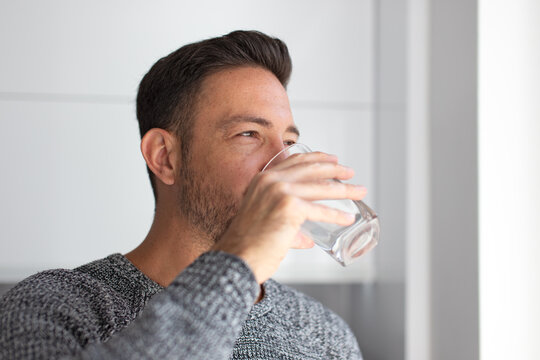 Man drink water from glass indoors looking away
