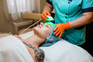 Beautiful female patient is getting a face skin treatment while lying at cosmeticians office, close up