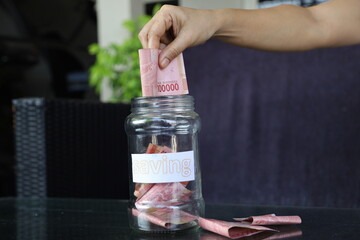 Woman holding dollar bills, on the table a large pile of coins and banks, she is managing to divide the money to save money and invest it to make it grow even more. Saving money and investing concept.