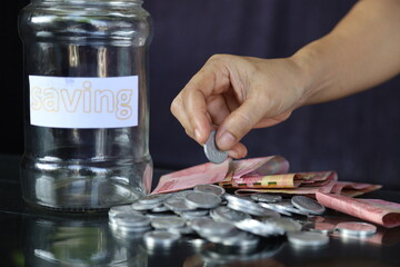 Woman holding dollar bills, on the table a large pile of coins and banks, she is managing to divide the money to save money and invest it to make it grow even more. Saving money and investing concept.