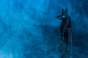 Egyptian statue of the god of death Anubis made of black stone in a blue fog