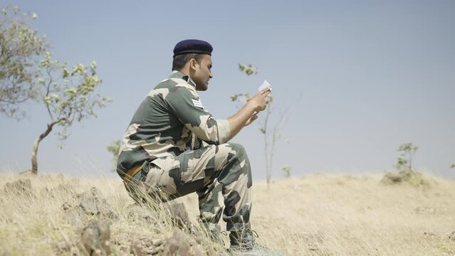 Young Indian Soldier Reading Letter Or Mail From Family Member While At Service On Top Of Mountian - Concept Of Missing Family, Bonding And Distant Communication