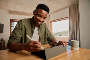 Happy young adult African American male writing with pen on electronic tablet while working remotely from apartment.