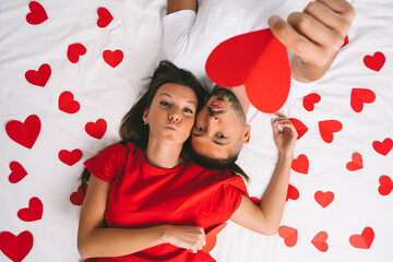 Top view of beautiful young couple in love lying on white bed with red hearts. Love and...