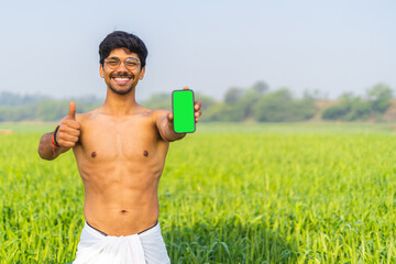 Indian indian farmer holding a mobile phone in his hands while standing in the fields. Mobile phone...