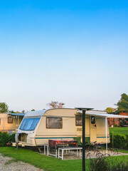 Cozy retro travel trailer Caravan on green grass before sunset near riverside in peaceful countryside. Family vacation travel RV, holiday trip in motorhome. Outdoor and Recreational Vehicles Theme.