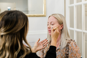 Cosmetologist applying foundation makeup to a blond woman in a makeup chair