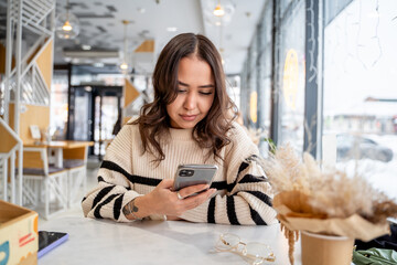 A young woman sits in a cafe and reads the news through her smartphone, emotions