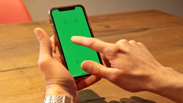 A man's hands holds a green screen smartphone, one touch with finger on the screen of the smartphone. Close-up.