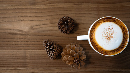 Cappuccino from top view with wooden table.Cup of coffee with copy space.Wood grain.
Milk froth floats on top of a cappuccino or latte.wood grain background and coffee cup
 with pine cone.