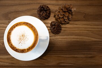 Cappuccino from top view with wooden table.Cup of coffee with copy space.Wood grain.
Milk froth floats on top of a cappuccino or latte.wood grain background and coffee cup
 with pine cone.
