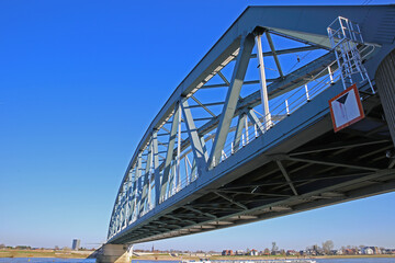 Nijmegen, Netherlands - February 27. 2022: View on truss railway bridge over river waal against blue sky