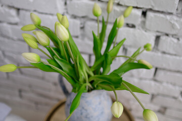 Vase with yellow tulips on a wooden bedside table.