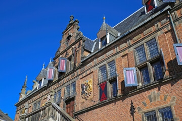 Fototapeta na wymiar Nijmegen, Netherlands - February 27. 2022: Low angle view on medieval renaissance red brick style facade against cloudless blue sky 