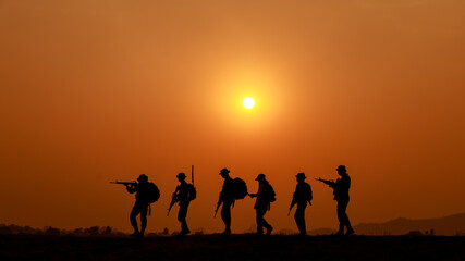Fototapeta na wymiar silhouette action soldiers walking and hold weapons background is sunset white balance ship effect