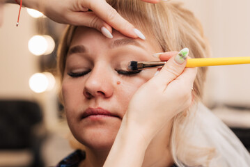A woman's hand applies eye shadow with a makeup brush.
