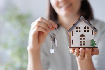 a woman realtor or mortgage agent holds a miniature of the house and keys in her hands. sale and purchase of real estate apartments or houses with a garden. conclusion of a dogvor for the rental of