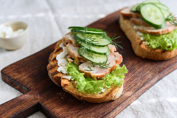 Sandwiches with chicken meat, cucumber, lettuce  and soft cheese on wooden board. Selective focus
