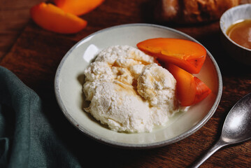 Homemade ricotta cheese or cheese curd served with fresh persimmon and honey and croissante on wooden background. Healthy breakfast. Haze effect. Selective focus