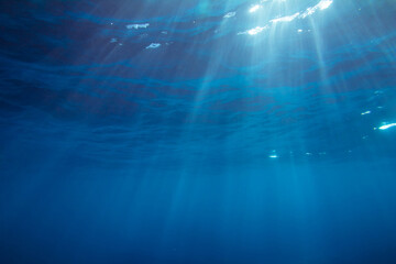Deep blue tropical ocean underwater photo with sun rays