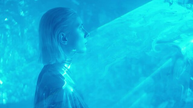 Alien woman in shiny silver dress walking through liquid sky laser light projection in dark studio
