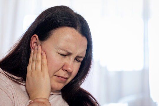 Pretty young woman suffering to strong tinnitus disease, sick female having an ear pain touching her painful head, healthcare concept