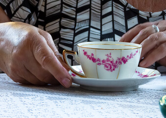 Woman hand holding a tea cup on a table with white lace tablecloth. She wears a black and white blouse and a silver ring
