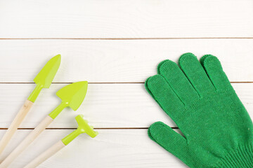 Garden supplies:shovels, rakes; green gardening gloves on a white wooden background.Gardening...