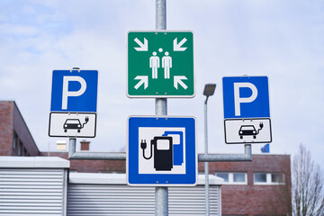 Electric car parking lot sign with charging station sign. Assembly point sign in the middle.