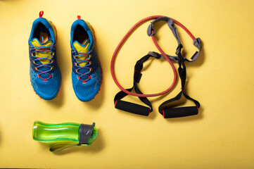 Running shoes and rubber bands for fitness. Cardio with rubber expander. Yellow background. Top view.