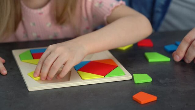 Close up of childrens hands put colored tangram puzzle. Family spends leisure time collect wooden jigsaw. Education concept.