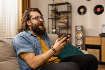 A bearded man full of excitement wins a round of favorite computer game on a console. The happy...