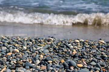 Fototapeta na wymiar Various stones and pebbles in front of blurry foamy sea wave at the beach in sunlight