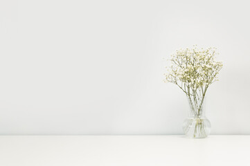 Bouquet of white pastel flowers gypsophila in a vase on table against the background of a white wall. Minimalistic scandinavian background mockup with copy space.