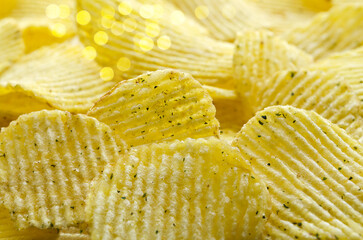 Defocused background with delicious corrugated potato chips with herbs. Selective focus