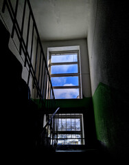 old entrance of a multi storey building in Russia is a view from the inside and a look at the window at the blue sky and white clouds.