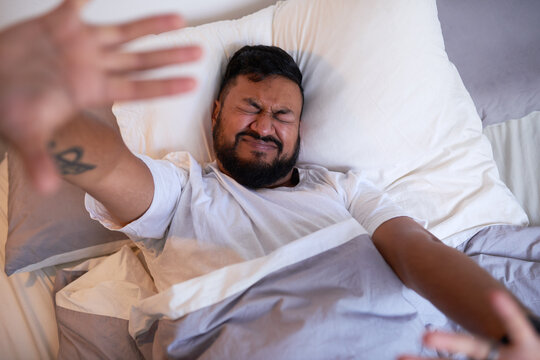 An Adult Man Stretches In Bed Struggling To Wake Up In The Morning