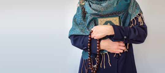 Portrait of Muslim woman holding Koran and rosary wears hijab. Islamic mockup background.