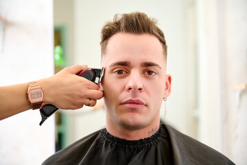 a man sitting in the barbershop while the hairdresser was styling his hair with an electric clipper