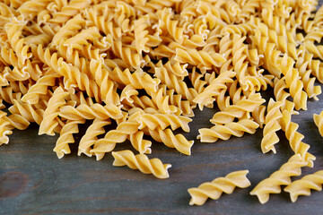 Heap of Uncooked Whole Wheat Fusilli Pasta on Back Wooden Backdrop