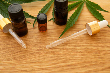 Medical cannabis oil concept image. Glass bottles and pipettes near natural cannabis leaves on wooden background