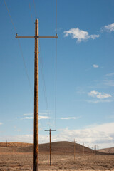 A row of power poles or telephone pole wires strung for miles across barren hilly land of Wyoming....