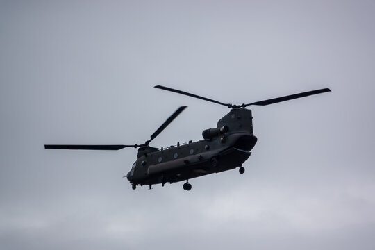 close up of an RAF Chinook CH-47 tandem-rotor helicopter flying low in a cloudy blue grey and white winter sky on a military exercise, Wiltshire UK