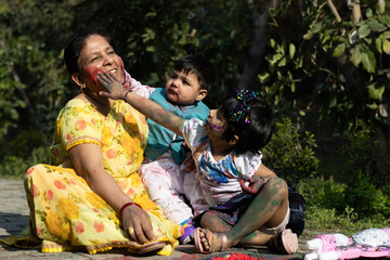 Happy Asian Indian Kids Boy, Girl And Grandmother Multi Generation Enjoying The Festival Of Colors With Holi Color Powder Called Gulal Or Rang