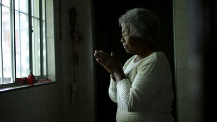 A contemplative senior black woman praying to God at home