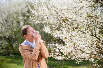 Woman allergic suffering from seasonal allergy at spring, posing in blossoming garden at...